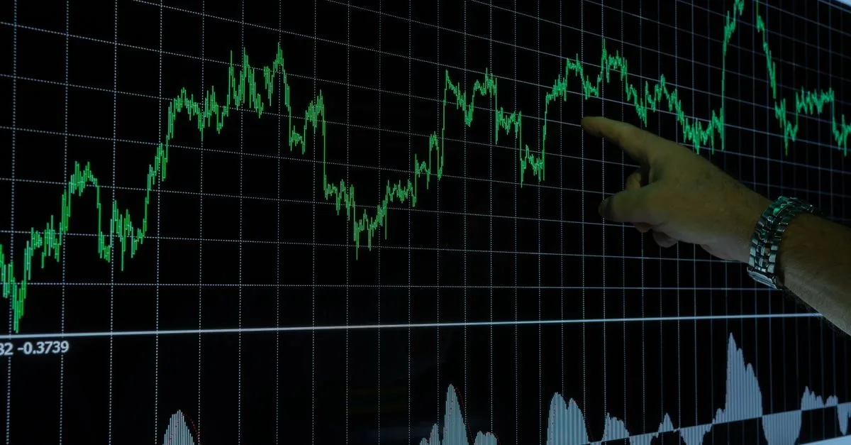 A hand points to a financial graph on a digital screen, indicating market trends.