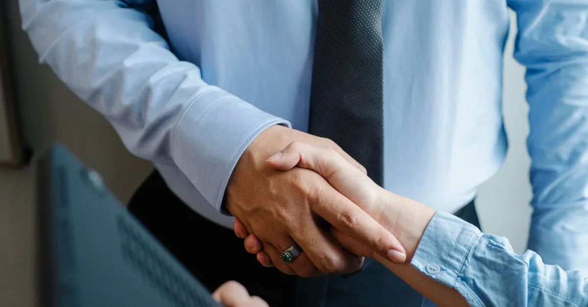 High angle of crop unrecognizable male and female business partners in formal clothes shaking hands after successful deal